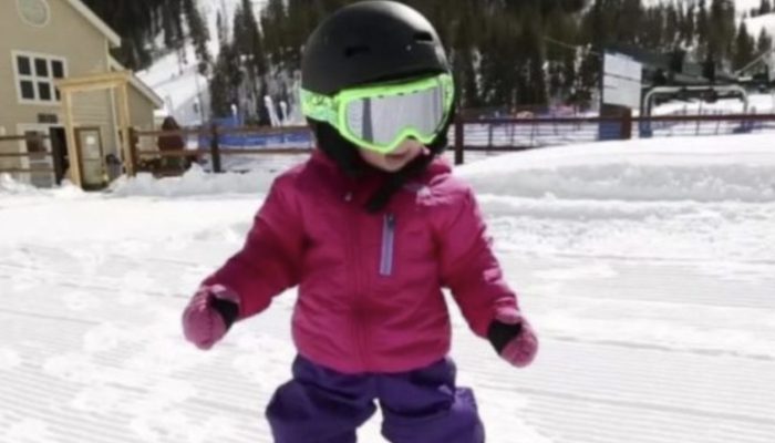 A precious 1-year-old child stands on a snowboard while maintaining great balance.