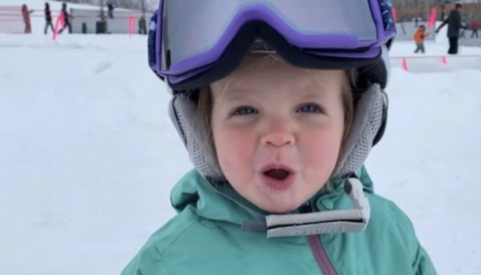 A precious 1-year-old child stands on a snowboard while maintaining great balance.