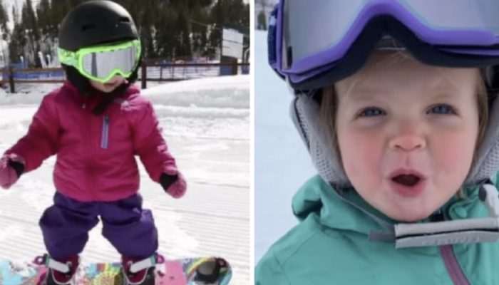 A precious 1-year-old child stands on a snowboard while maintaining great balance.